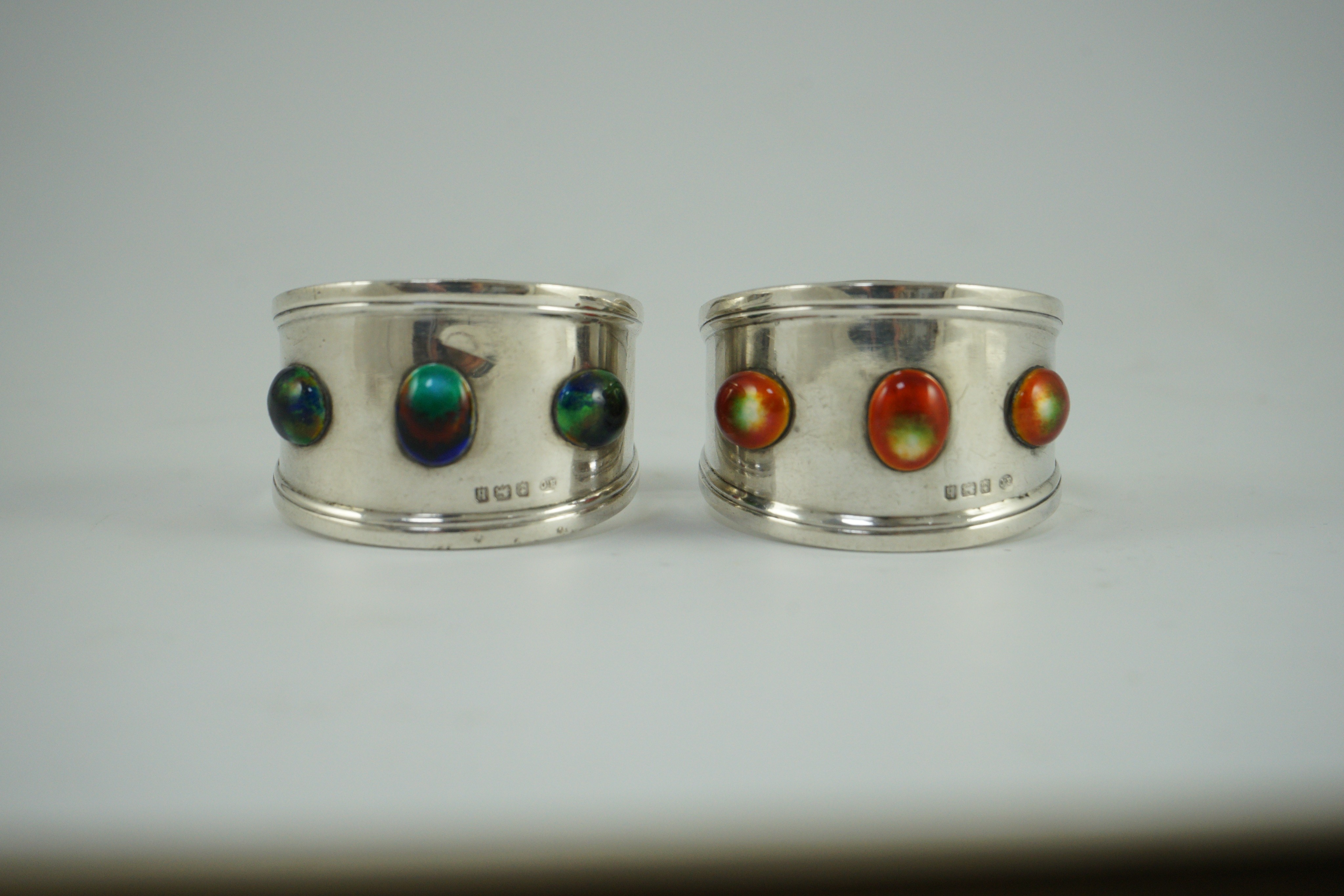 Two similar Edwardian Arts & Crafts silver and enamelled napkin rings